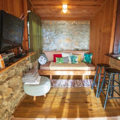 Interior of rustic house with counter placed near sofa with cushions and TV hanging on wooden wall near various supplies