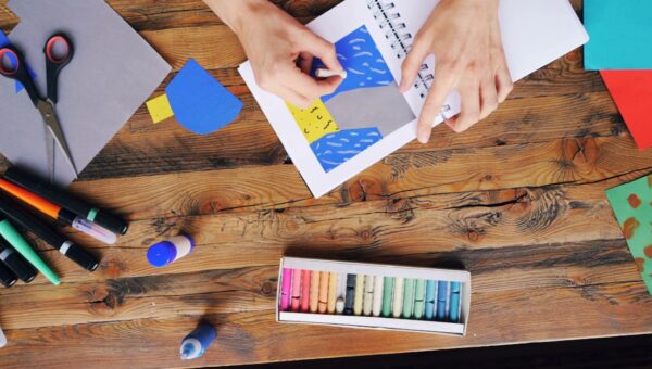 A vibrant arts and crafts setup with colorful papers and pastel colors on a wooden table.