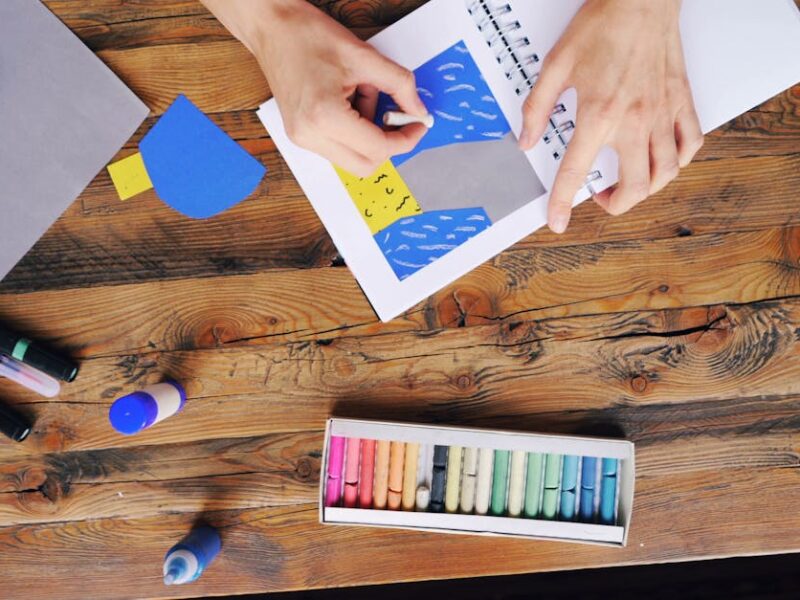 A vibrant arts and crafts setup with colorful papers and pastel colors on a wooden table.