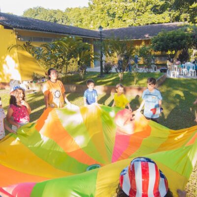 A joyful outdoor birthday party with children playing with a colorful parachute in a garden setting.