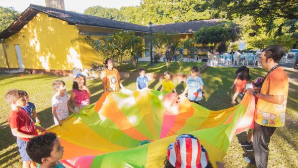 A joyful outdoor birthday party with children playing with a colorful parachute in a garden setting.
