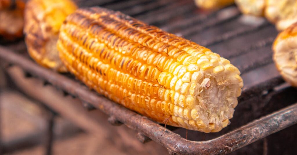 Close-up of grilled corn on the cob over a charcoal grill, capturing its golden texture and appetizing look.