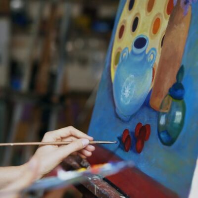 Close up of artist's hand painting a still life on canvas in a studio environment.