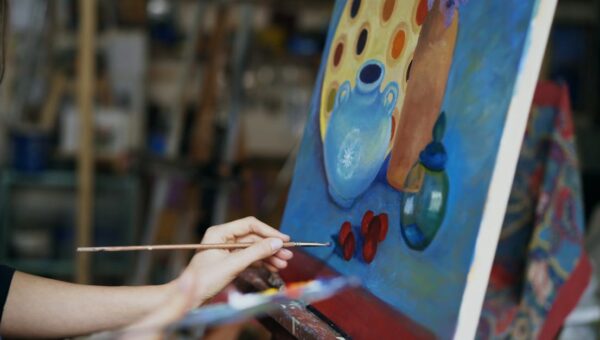 Close up of artist's hand painting a still life on canvas in a studio environment.