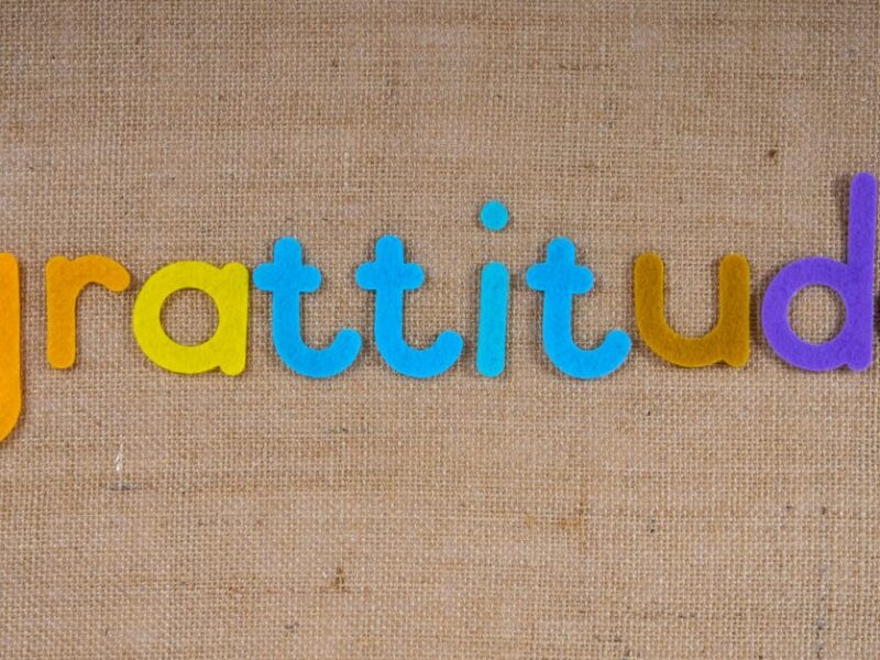 Vibrant colored letters spelling 'gratitude' on a textured burlap surface.