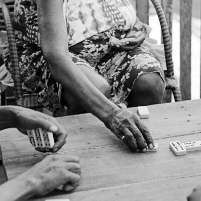 Black and white photo of people playing dominoes on a wooden table in Brazil.