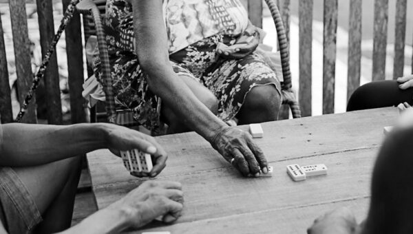 Black and white photo of people playing dominoes on a wooden table in Brazil.