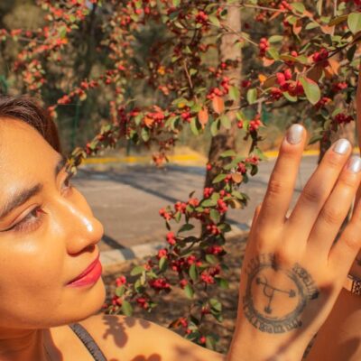 A stylish woman in nature appreciating a sunny day in Mexico City, surrounded by vibrant red berries.
