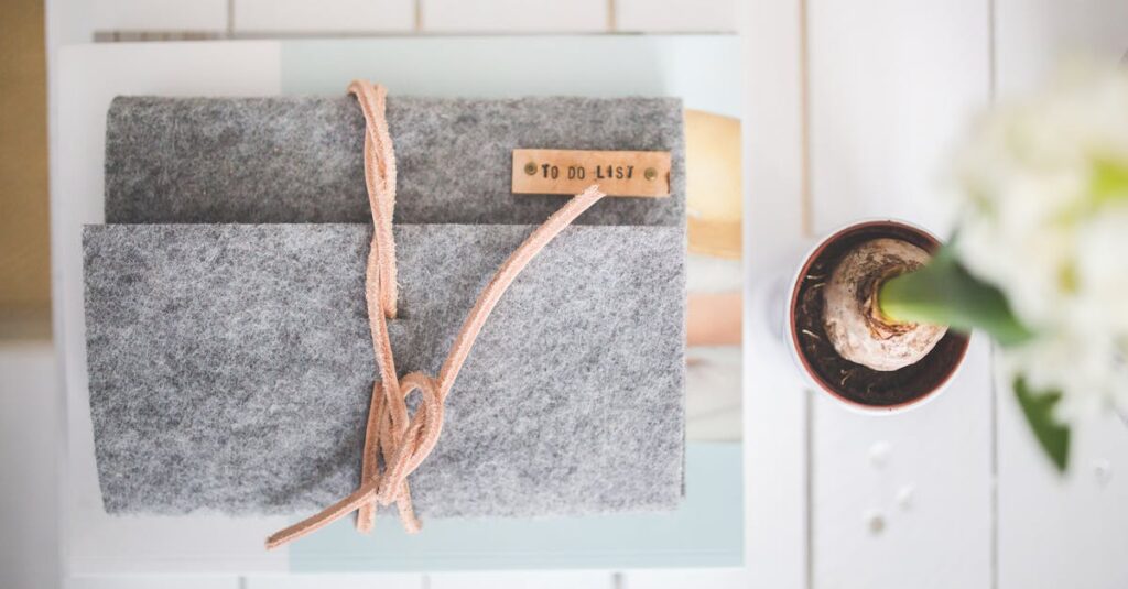 Flat lay of a gray felt notebook with a to-do list tag and a small potted plant on a white desk.