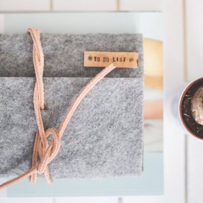 Flat lay of a gray felt notebook with a to-do list tag and a small potted plant on a white desk.