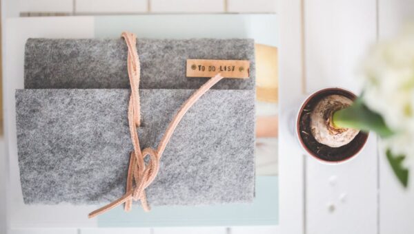 Flat lay of a gray felt notebook with a to-do list tag and a small potted plant on a white desk.