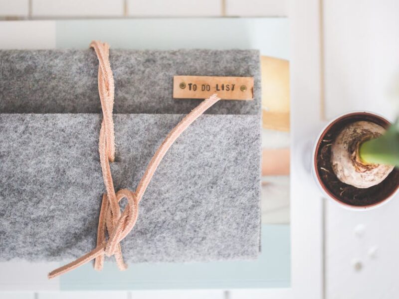 Flat lay of a gray felt notebook with a to-do list tag and a small potted plant on a white desk.