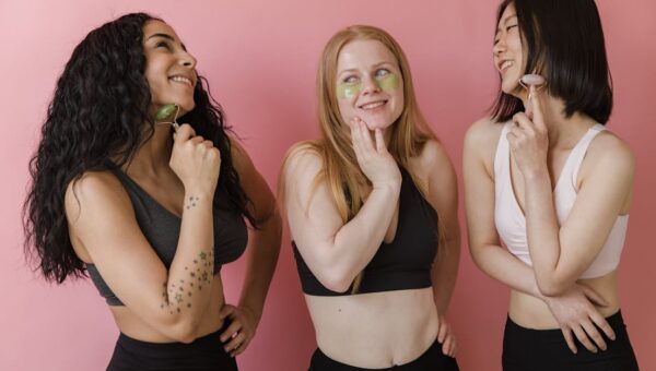 Three diverse women using jade rollers and face masks, enjoying a skincare routine.