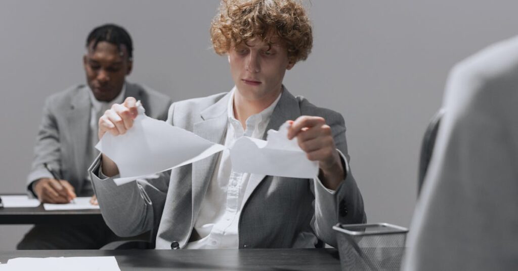 Two employees in suits sitting at desks, one tearing paper.