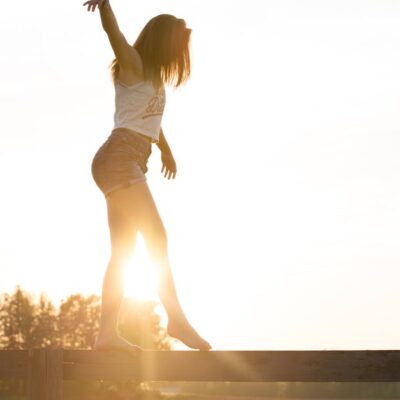 A young woman balancing on a fence during a serene sunrise, exuding freedom and joy.