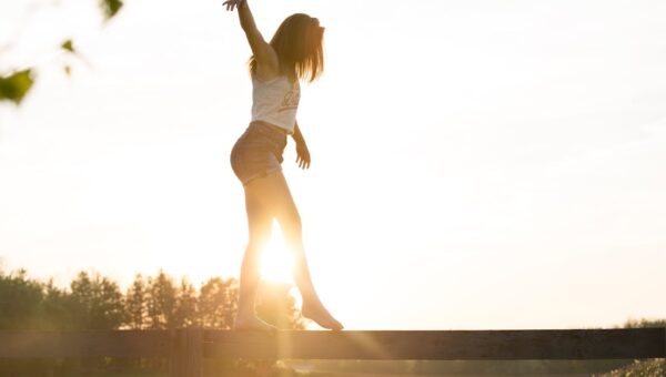 A young woman balancing on a fence during a serene sunrise, exuding freedom and joy.