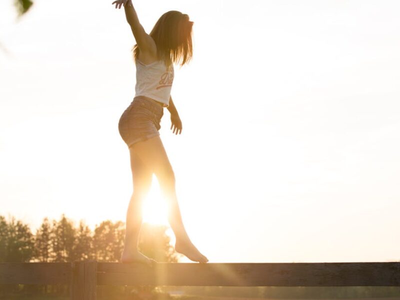 A young woman balancing on a fence during a serene sunrise, exuding freedom and joy.