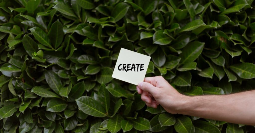 A hand holding a note with 'Create' written on it against a lush green leafy background.