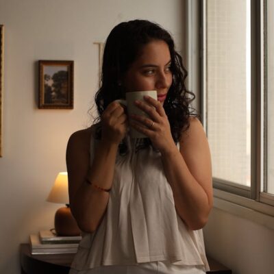 Young woman gazing out window with coffee, enjoying morning indoors.