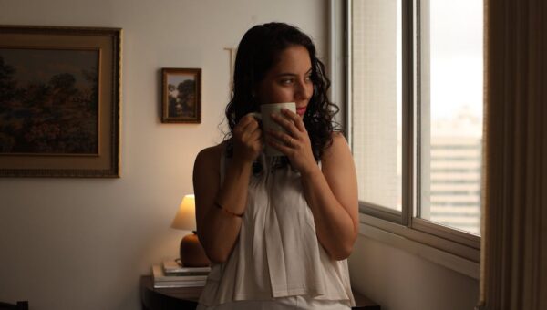 Young woman gazing out window with coffee, enjoying morning indoors.