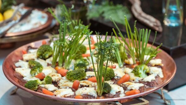 An artistic presentation of vegetables including broccoli, carrots, and greens on a copper platter.