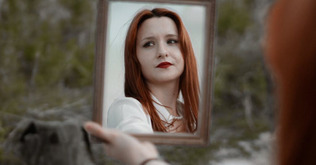 A young redhead woman holding a mirror outdoors, showcasing her reflection with red lips.