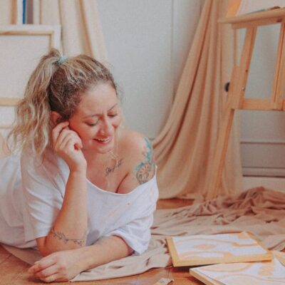 Smiling woman relaxing and creating art in a cozy room with canvases and paints.