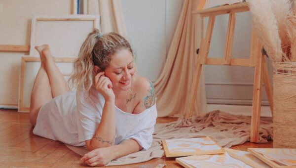 Smiling woman relaxing and creating art in a cozy room with canvases and paints.