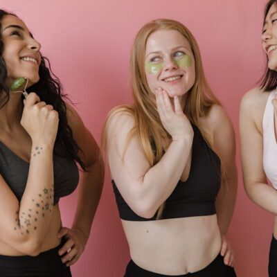 Three diverse women using jade rollers and face masks, enjoying a skincare routine.