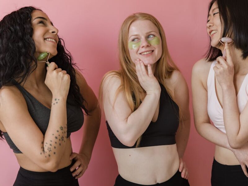 Three diverse women using jade rollers and face masks, enjoying a skincare routine.