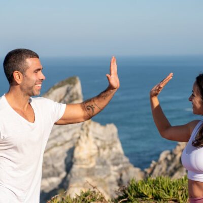Fit couple in athletic wear high-fiving by the sea on a sunny day in Portugal.