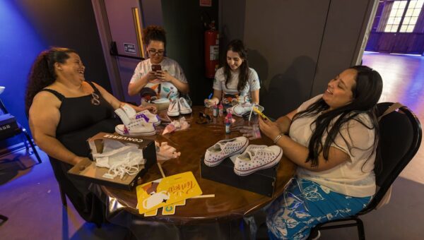 A group of women creatively painting sneakers at an indoor art workshop, showcasing teamwork and creativity.
