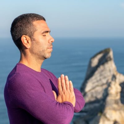 Side view of a man meditating by the ocean cliffs in Portugal, promoting relaxation and mindfulness.
