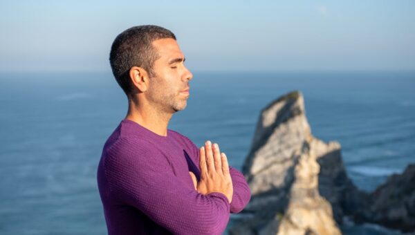 Side view of a man meditating by the ocean cliffs in Portugal, promoting relaxation and mindfulness.