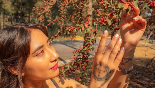 A stylish woman in nature appreciating a sunny day in Mexico City, surrounded by vibrant red berries.