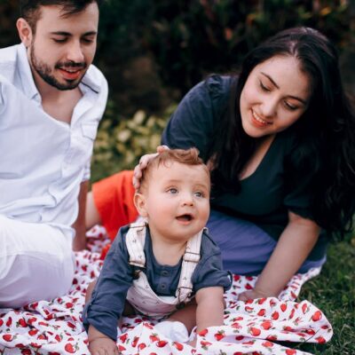 A joyful family enjoying a picnic outdoors during summer. Smiling parents with their baby on a blanket.