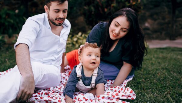 A joyful family enjoying a picnic outdoors during summer. Smiling parents with their baby on a blanket.