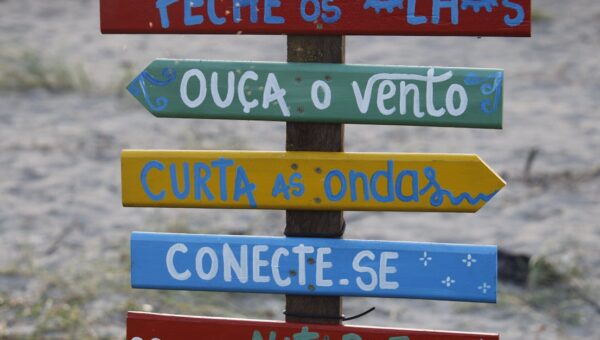 Vibrant wooden sign with motivational phrases on a beach in Guaratuba, Brazil.