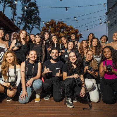 A diverse group of photographers pose outdoors at a photography meetup, showcasing their cameras.