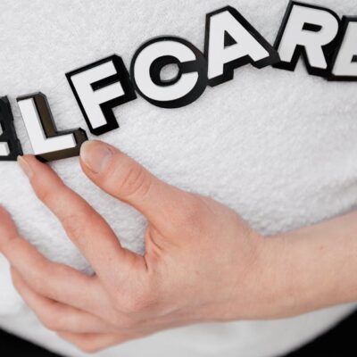 Close-up of a hand holding the word 'self-care' made with 3D letters on a white background.