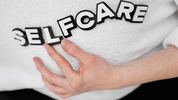 Close-up of a hand holding the word 'self-care' made with 3D letters on a white background.