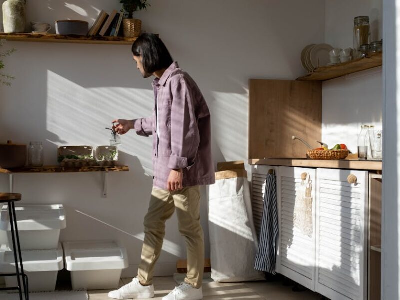 Man in casual wear tending to indoor plants in a sunlit kitchen.