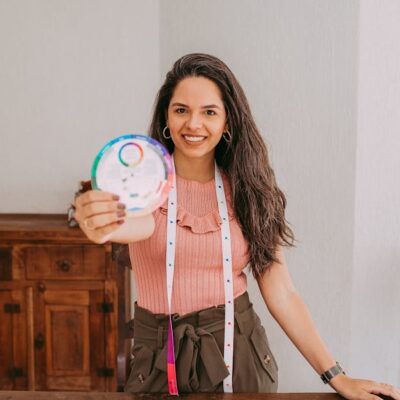 Smiling woman displaying a color wheel at a table with fabric samples in a workshop setting.