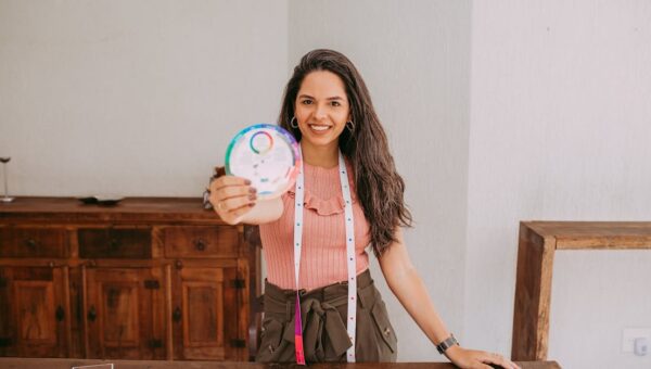 Smiling woman displaying a color wheel at a table with fabric samples in a workshop setting.