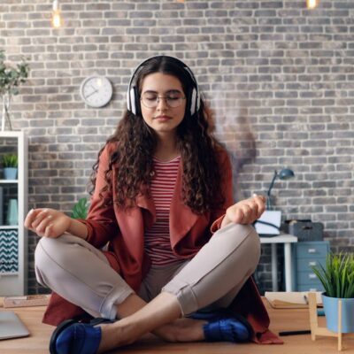 Young woman meditating with headphones in a modern office setting, practicing mindfulness.