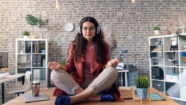 Young woman meditating with headphones in a modern office setting, practicing mindfulness.