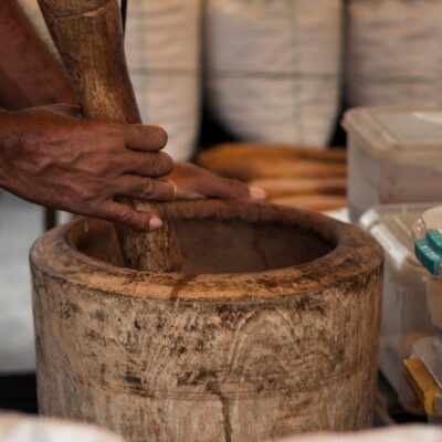 Close-up of hands grinding herbs in a wooden mortar at a São Paulo market stall.