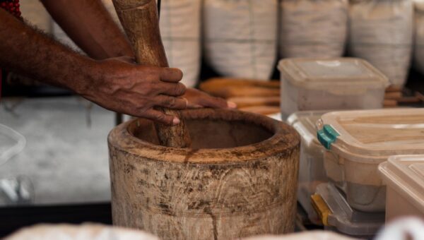 Close-up of hands grinding herbs in a wooden mortar at a São Paulo market stall.