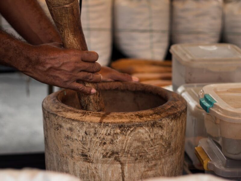 Close-up of hands grinding herbs in a wooden mortar at a São Paulo market stall.