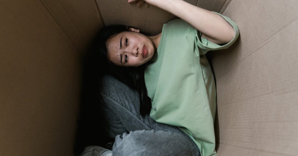 Woman enclosed in a cardboard box, showing signs of stress and fear.